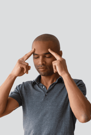 Man with eyes closed touching his temples with both hands, appearing focused or concentrating, against a plain background.