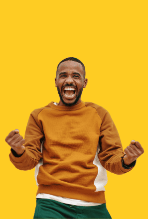 Man celebrating with arms raised and fists clenched, smiling excitedly, wearing a brown sweatshirt against a bright yellow background.
