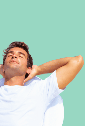 Man reclining with hands behind his head and eyes closed, appearing relaxed and calm against a light green background.