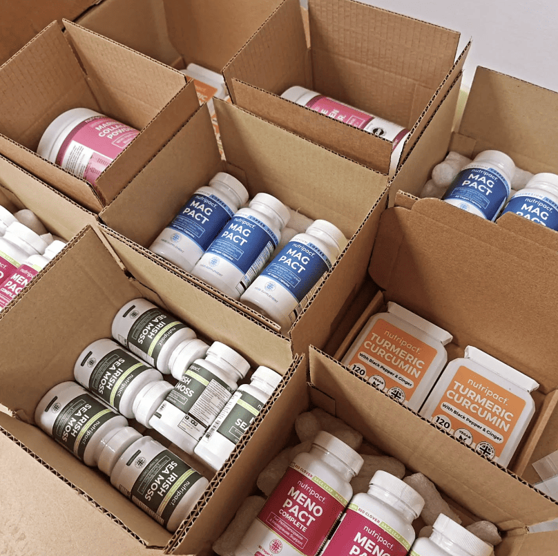 Open cardboard boxes filled with Nutripact supplement products, including Magnesium Complex Capsules, Turmeric Complex Capsules, Sea Moss Complex Capsules, and Perimenopause & Menopause Capsules bottles, packed with protective filler for shipping.